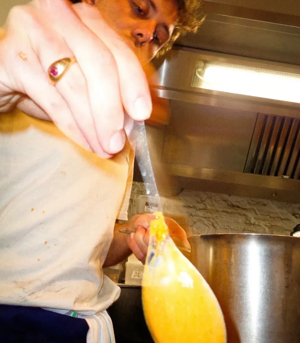 Un cuisinier de Mammouth goûte une sauce orangée à la louche au-dessus de la marmite, sous la hotte