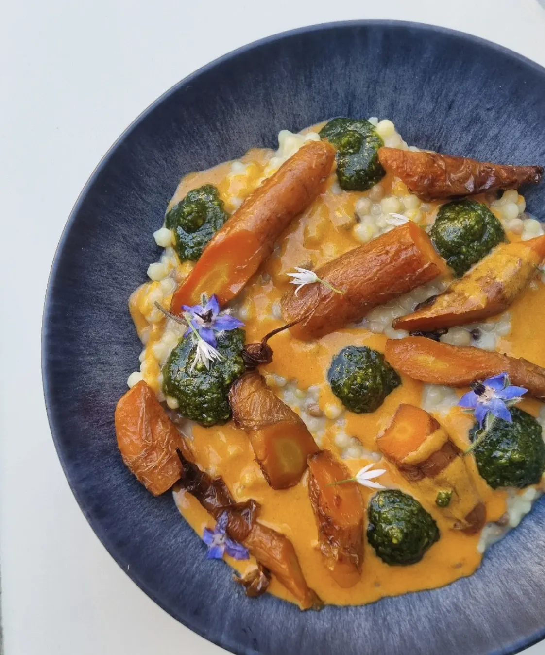 Une assiette de carottes rôties, sauce et fleurs dans une assiette bleue chez Mammouth