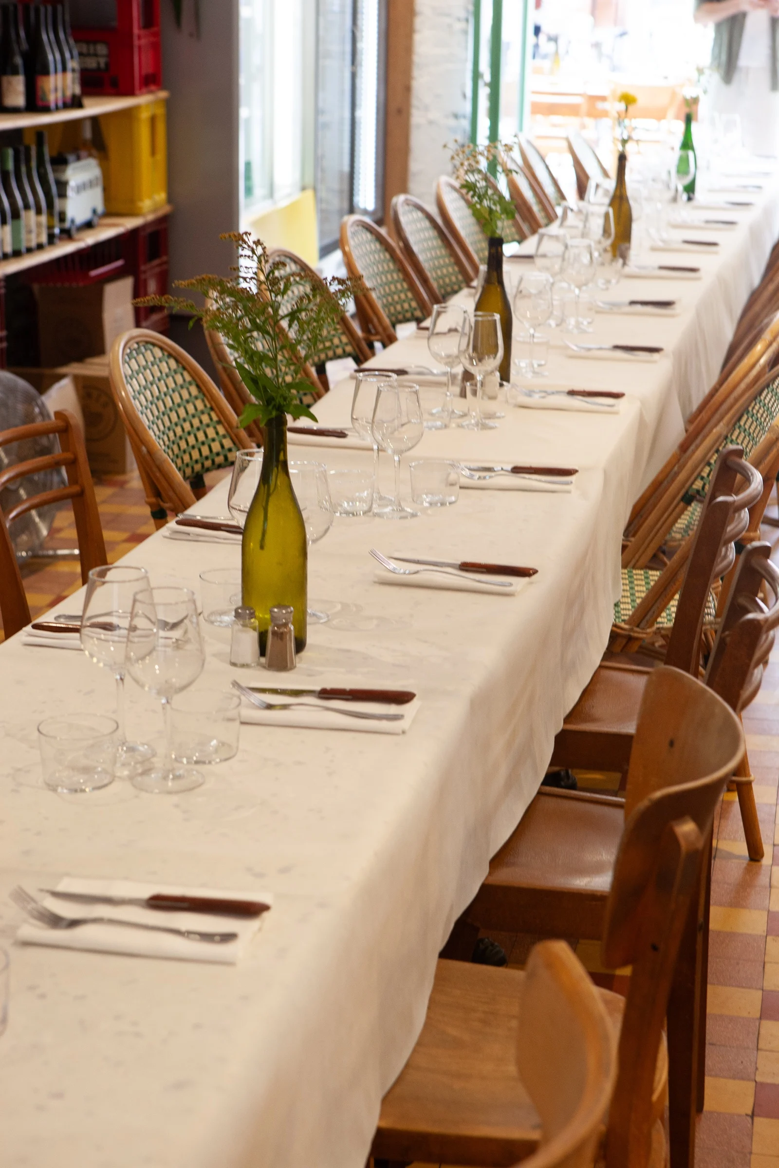 La grande table de Mammouth dressée en nappe blanche, chaises en rotin, verres et bouteilles fleuries