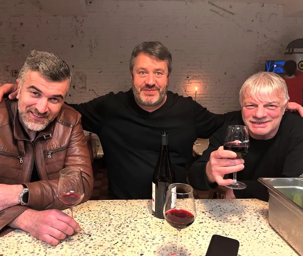 Trois amis de la maison attablés au comptoir en terrazzo de Mammouth, verres de vin rouge à la main